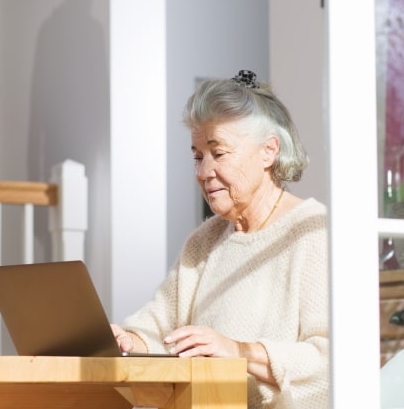 femme cheveux gris sur un table en train de taper sur un ordinateur