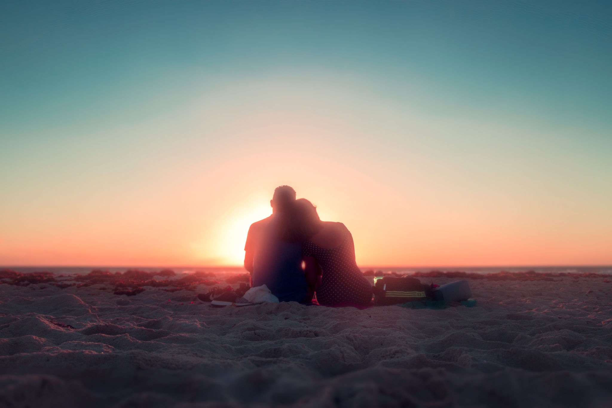 Pareja de enamorados sentados en la playa mirando el amanecer