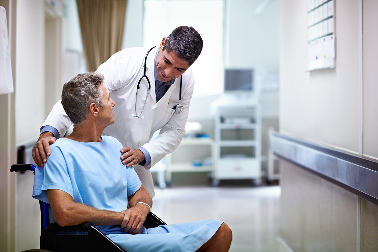 Shot of a doctor talking to a patient in a wheelchair in a hospital corridor