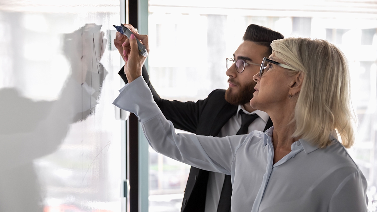 Concentrated diverse businesspeople write on whiteboard engaged in creative thinking together, focused multiracial colleagues brainstorm develop business strategies on flip chart, teamwork concept